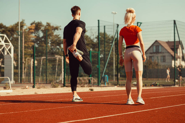 dziewczyna i facet robi rozgrzewkę przed ćwiczeniami sportowymi na stadionie - Zdjęcie, obraz
