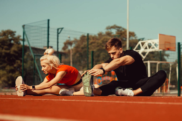 girl and a guy doing a warm-up before sports exercises at the school stadium - Фото, зображення