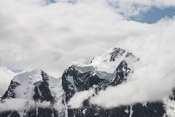 Atmosferik minimalist alp manzarası karlı dağ zirvesinde asılı devasa bir buzulla. Buzul sınırında büyük bir balkon. Karlı dağların arasında alçak bulutlar. Yüksek irtifada görkemli manzara. - Fotoğraf, Görsel