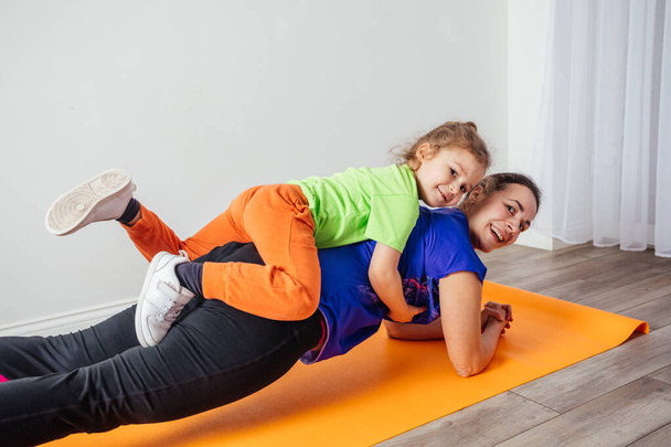 Active boy laying on his mother while she is standing in plank - Фото, зображення
