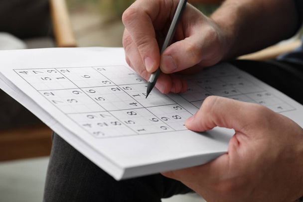 Man solving sudoku puzzle indoors, closeup view - Фото, зображення