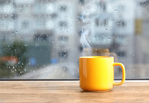 Cup of hot drink near window on rainy day. Space for text - Foto, Imagen