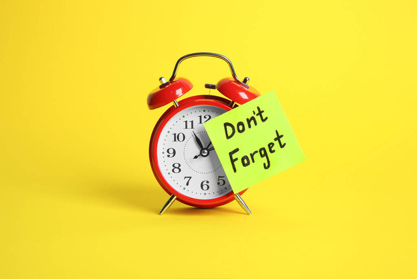 Alarm clock and reminder note with phrase Don't forget on yellow background - Photo, image
