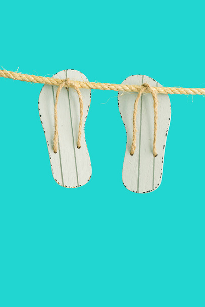 Summer concept, grey toy flip-flops hanging on rope with  turquoise color background. Bright summer minimal style. - Фото, изображение