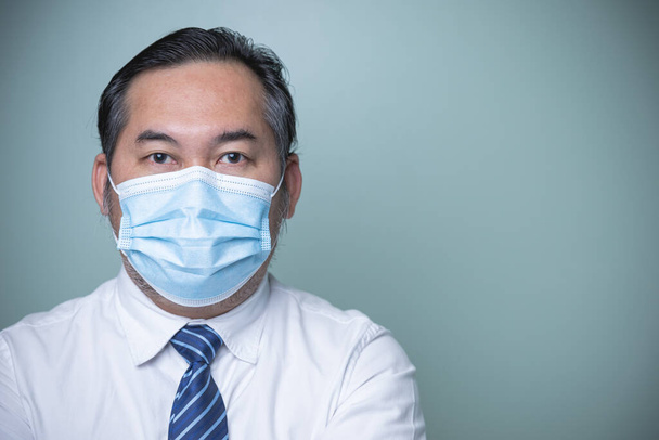 İş adamı mavi kravatlı beyaz bir gömlek giyiyor ve mavi tıbbi maske takıyor. Koronavirüsü kopyalamak için kameraya bakıyor. Kavram, virüsü, yeni-normal, sosyal mesafeleri korur. - Fotoğraf, Görsel