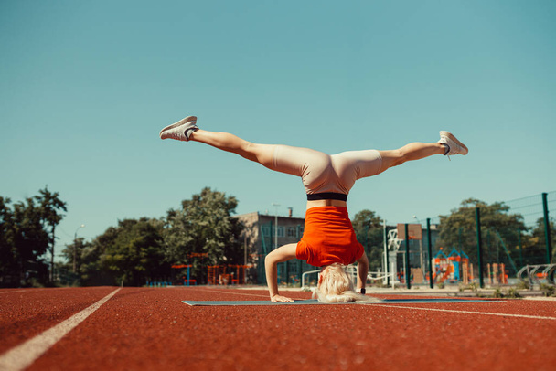 νεαρή ξανθιά μαθαίνει να ισορροπεί σε μια βάση κεφαλής και handstand - Φωτογραφία, εικόνα