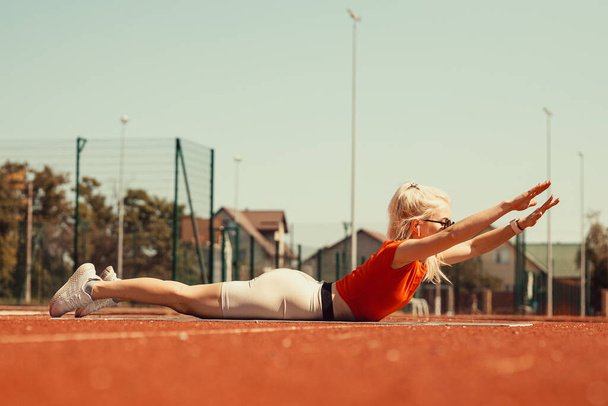 jeune blonde secoue les muscles abdominaux sur un tapis de sport dans la rue - Photo, image