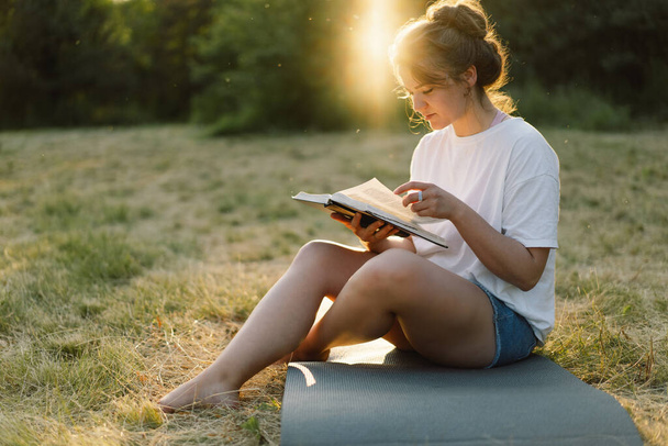 Χριστιανή γυναίκα κρατά τη Βίβλο στα χέρια της. Διαβάζοντας την Αγία Γραφή σε ένα χωράφι κατά τη διάρκεια του όμορφου ηλιοβασιλέματος. - Φωτογραφία, εικόνα