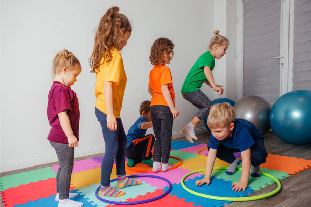 Children running and jumping around multicolor hoops on a floor - Foto, afbeelding