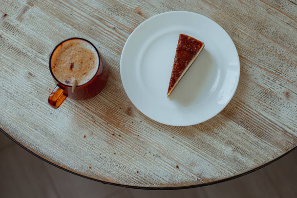 Καφές σε ένα γυάλινο κύπελλο και nutty cheesecake σε ένα λευκό πιάτο σταθεί σε ένα ξύλινο τραπέζι. - Φωτογραφία, εικόνα