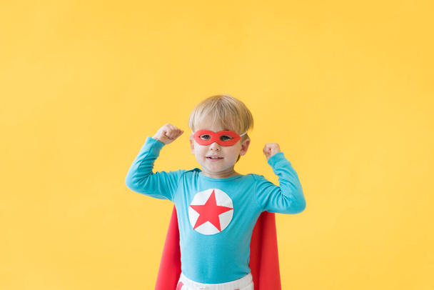 Superhero child against yellow paper background. Super hero kid wearing red mask and cape. Childhood dream and imagination concept - 写真・画像