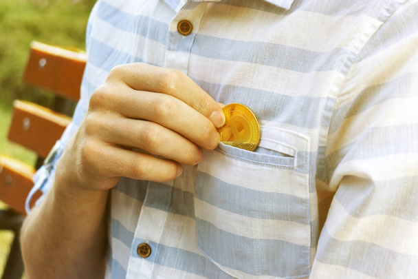 La mano de un hombre pone una moneda Dogecoin en su bolsillo en un primer plano sobre un fondo natural - Foto, Imagen