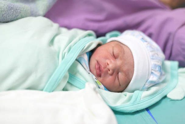 Ένα νεογέννητο μιας ημέρας: Ένα νεογέννητο μωρό βρίσκεται σε ένα κρεβάτι μωρού αφού μόλις γέννησε σε μια αίθουσα τοκετού νοσοκομείου. επιλεκτική εστίαση. - Φωτογραφία, εικόνα