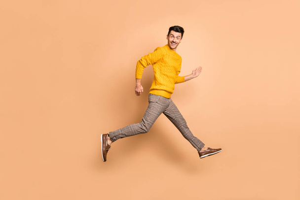 Full length photo portrait side profile of man running jumping up isolated on pastel beige colored background - Zdjęcie, obraz