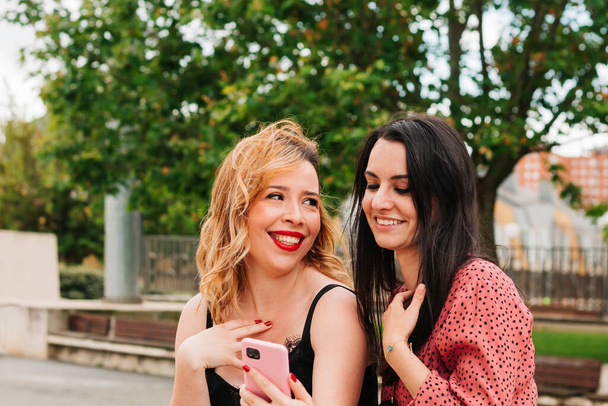 Due donne sorridenti che parlano e ridono per strada guardando il loro smartphone. concetto di felicità e stile di vita e amicizia - Foto, immagini