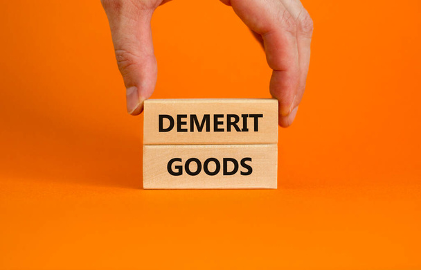 Demerit goods symbol. Wooden blocks with words Demerit goods on beautiful orange background, copy space. Businessman hand. Business and demerit goods concept. - Фото, изображение