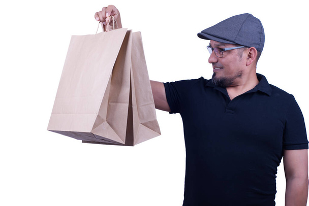 Man on a white background in a cap and glasses, lifts up some paper bags with purchases. - Photo, Image