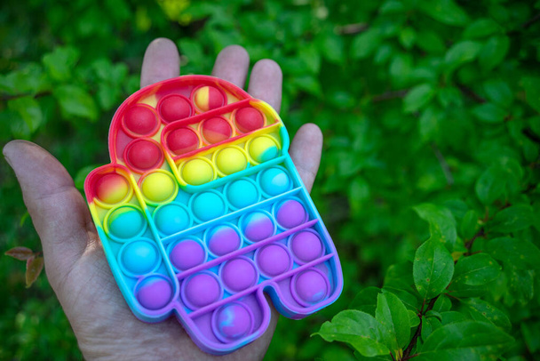 Το χέρι κρατά ένα ουράνιο τόξο χρώματος popit αντι-στρες παιχνίδι με τη μορφή ενός άνδρα - Φωτογραφία, εικόνα