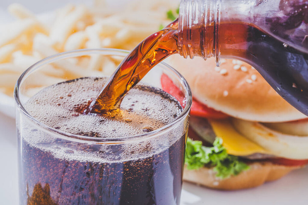 Bevanda analcolica versando in un bicchiere con hamburger su sfondo bianco - Foto, immagini