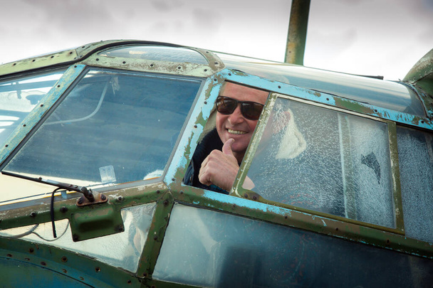 Ένας μεσήλικας πάνω σε ένα παλιό εγκαταλελειμμένο σοβιετικό αεροπλάνο. Ο άνθρωπος κοιτάζει έξω από το παράθυρο.. - Φωτογραφία, εικόνα