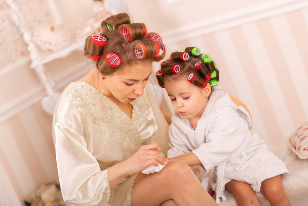 Adorable little girl with her mother in curlers paint their fingernails. Copies mom's behavior. Mom teaches her daughter to take care of herself. Beauty day. - Fotoğraf, Görsel