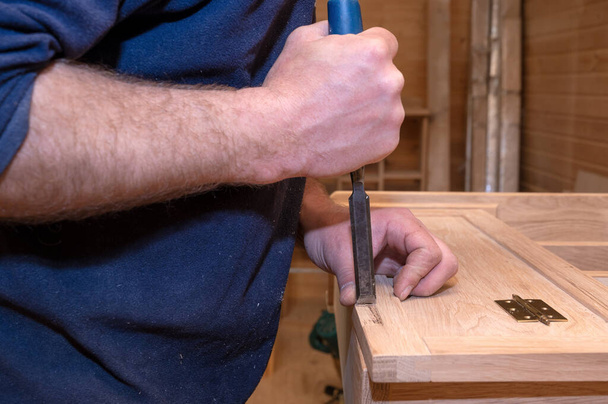 master carpenter works with a hand tool with a chisel, sets the hinges on the cabinet. Production of handmade wooden furniture. Selective focus close-up - Fotó, kép