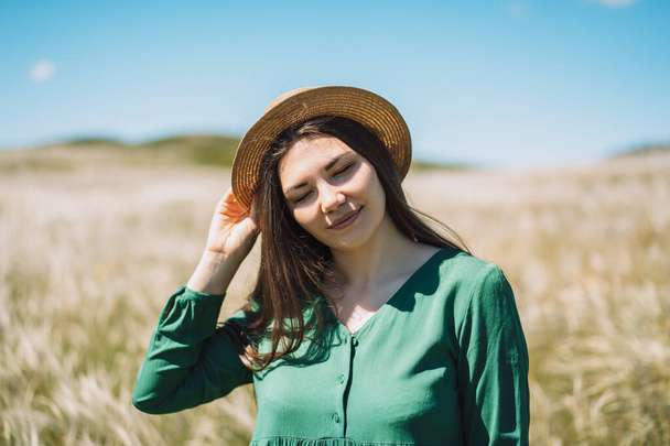 Νεαρή κοπέλα με πράσινο φόρεμα και ψάθινο καπέλο στο φόντο του γηπέδου. - Φωτογραφία, εικόνα