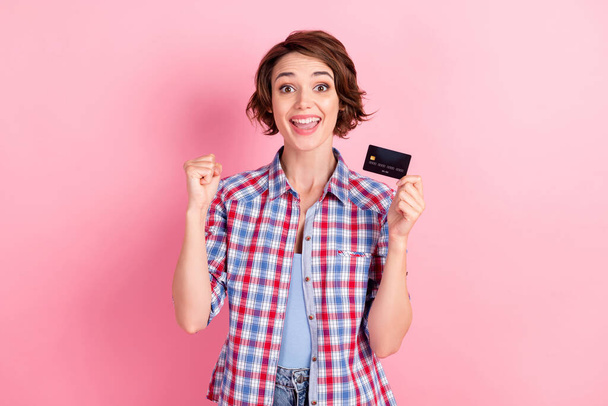 Photo of beaming lucky woman wear checkered shirt holding bank card hand arm fist isolated pink color background - Fotoğraf, Görsel