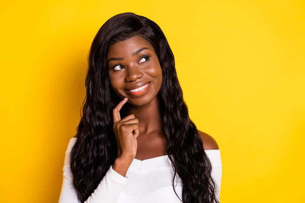 Photo portrait of black skinned woman curious looking blank space touching chin smiling isolated on vivid yellow color background - Fotó, kép