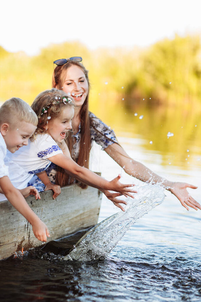junge schöne Mutter, die Zeit mit Kindern im Boot auf dem See im Park verbringt. Muttertag. Frauentag. Sohn und Tochter mit Wasser bespritzt. - Foto, Bild
