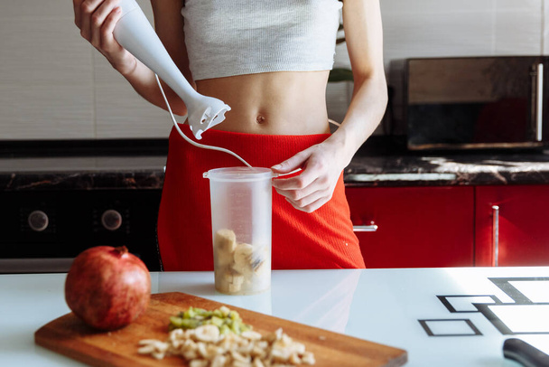 甘いバナナタンパク質ミルクシェイクを作る手ブレンダーを持つ女性。ジムの後のスポーツ栄養ダイエット。健康的なライフスタイル - 写真・画像
