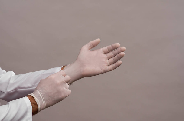 the doctor puts on disposable rubber protective gloves. close-up on a gray background.  - Fotoğraf, Görsel