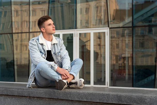 Urban portrait of a stylish guy against the backdrop of the glass facade of the building.H andsome young man resting on the street. - Valokuva, kuva
