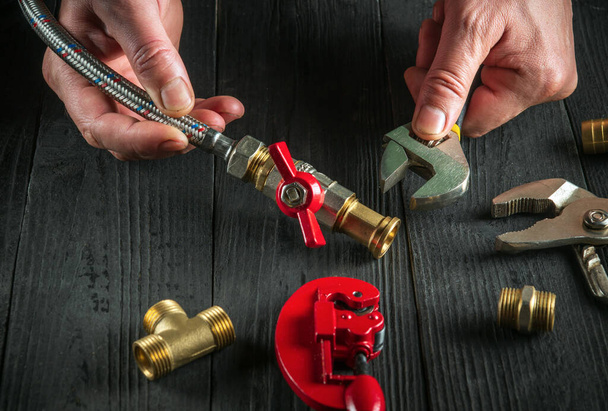 Klempnermeister verbindet Messingarmaturen, während er Geräte repariert. Nahaufnahme der Hände des Meisters bei der Arbeit in der Werkstatt. - Foto, Bild