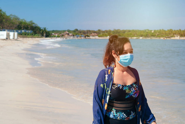 Donna matura con maschera protettiva cammina sulla spiaggia - Foto, immagini