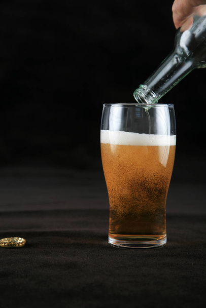 Een biertje. Een glas bier. Een glas bier op een zwarte achtergrond. bierglas met schuim. koud bier. Biermok. biermok.  - Foto, afbeelding