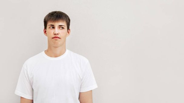 Young handsome man with short haircut. Portrait of fellow in white T-shirt on grey wall background. Caucasoid looks in right side. Copy space. - Foto, Imagem