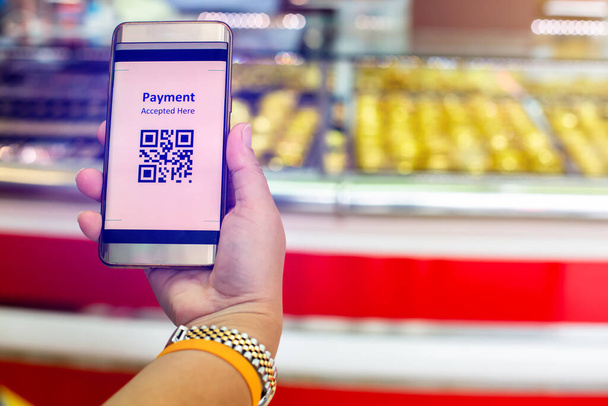 Selektive Fokussierung auf QR-Code-Tag auf dem Smartphone in der Hand des Kunden mit verschwommenem Goldschmuck Shop zu akzeptieren generieren digitales Bezahlen ohne Geld. Qr-Code-Bezahlkonzept. - Foto, Bild