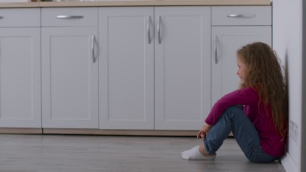 Solitaria niña abandonada sentada en el suelo de la cocina, escondiéndose de sus padres que discuten, sintiéndose asustada y estresada - Imágenes, Vídeo