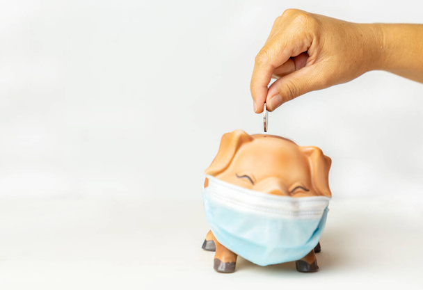 The woman put coin in piggy bank wearing surgical mask isolated on a white background. - Photo, Image