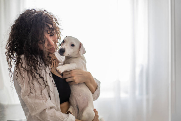 Happy curly brunette woman pet owner holding dog Jack Russell Terrier breed feeling love friendship - Fotó, kép