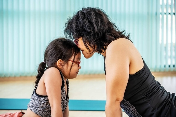 Азиатская мать с маленькой дочерью улыбаются, практикуя йогу вместе дома, упражнения класса на коврике asana дома. родители сопровождают здоровых детей спортивная концепция - Фото, изображение