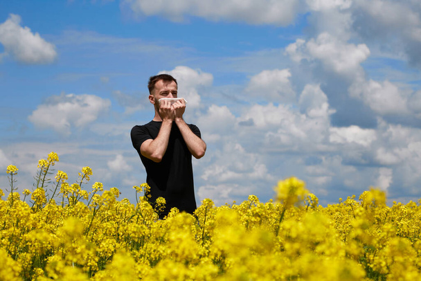 El hombre es alérgico al polen de las plantas en flor. Estornuda, cubriéndose la boca con una servilleta. - Foto, imagen