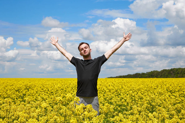 Młody pozytywny facet stoi na żółtym polu, radując się i wyciąga ręce do nieba.. - Zdjęcie, obraz