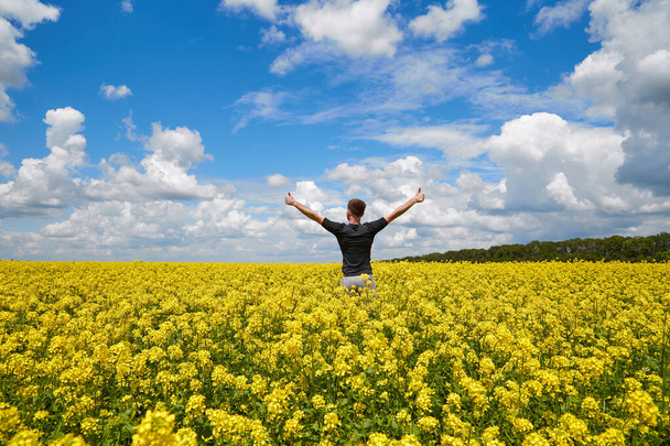 A happy farmer stands in a rapeseed field with his hands up. - Photo, Image