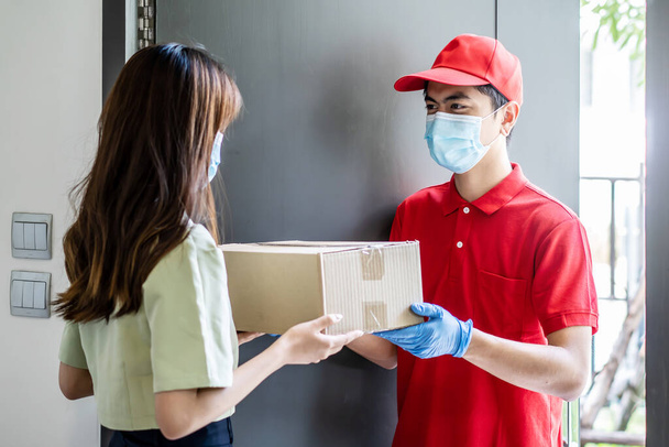 Delivery man in red uniform holdinging parcel boxes to a woman customer - courier service concept - Фото, изображение