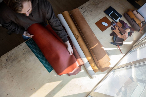 Craftsman unwrapping bundle of stuff natural material working at leather workshop. Leatherwork - 写真・画像