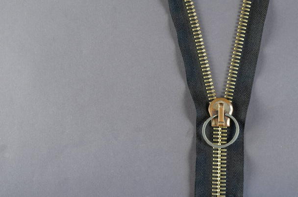 Metal zipper on gray background. Clasp with yellow prongs and black braid. Copy space. Top view. - Photo, Image