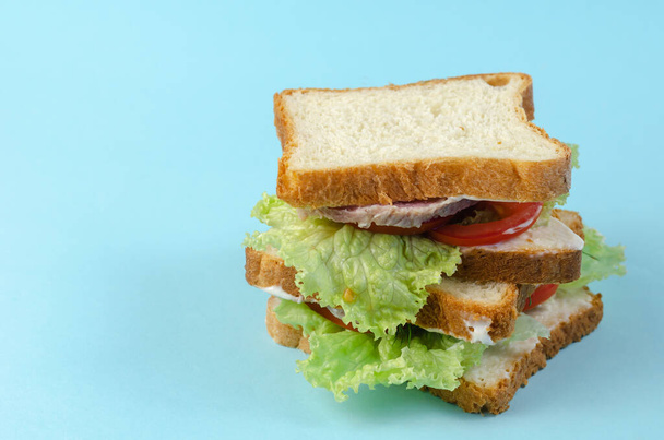 Ready-to-eat food on a light blue background. A stack of appetizing sandwiches with chopped ham, tomatoes, dill, lettuce, and white sauce. Side view. - Photo, image