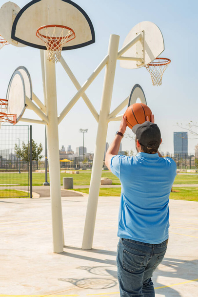 A back view of a young man playing basketball in a sports park - Фото, зображення